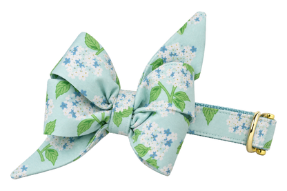 Dog collar featuring a large belle bow in Blue Hydrangeas fabric, a pale aqua print with blue hydrangea blooms, attached to a matching Blue Hydrangeas collar with a nylon inner lining and gleaming gold hardware, including a D-ring and buckle.