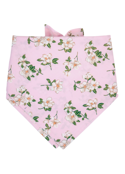 Dog bandana in a soft pink fabric with clusters of white magnolia flowers and leaves. The bandana is folded in a classic triangular shape with neatly stitched edges and ties at the back of the neck. Lightweight and elegant, it offers a romantic, feminine accessory for pets, coordinating with the matching collar and leash in the same floral design.