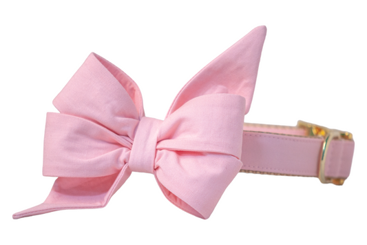 Elegant pink fabric dog collar with a voluminous decorative belle bow that has flared tails and a tailored center, finished with gleaming gold metal accents.