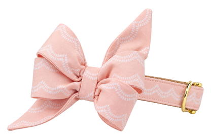 Dog collar featuring a large belle bow in Blush Waves fabric, a blush peach pink fabric with thin white scalloped wave lines, attached to a matching Blush Waves collar with a nylon inner lining and gleaming gold hardware, including a D-ring and buckle.