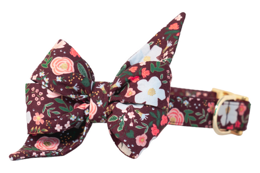 Dog collar with a large pointed fabric belle bow, both in a dark burgundy pattern with blossoms, roses, flowers, and foliage, finished with a shiny buckle and hardware.