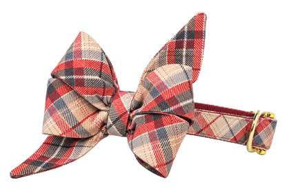 Dog collar featuring a large belle bow in Burbank Plaid fabric, a tan and cream plaid with coral red and charcoal stripes, attached to a matching Burbank Plaid collar with a nylon inner lining and gleaming gold hardware, including a D-ring and buckle.