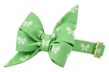 Dog collar featuring a large belle bow in Butterfly Fields fabric, a soft spring green fabric with small white butterflies, attached to a matching Butterfly Fields collar with a nylon inner lining and gleaming gold hardware, including a D-ring and buckle.