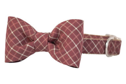 Classic-style dog collar in a burgundy and plaid print, with a matching bow tie attached at the front. The bow ties' clean folds mirror the crisp check pattern of the collar strap. Hardware includes a shiny D-ring for leash attachment and a matching adjustable buckle. The overall design blends polished formality with everyday wearability.