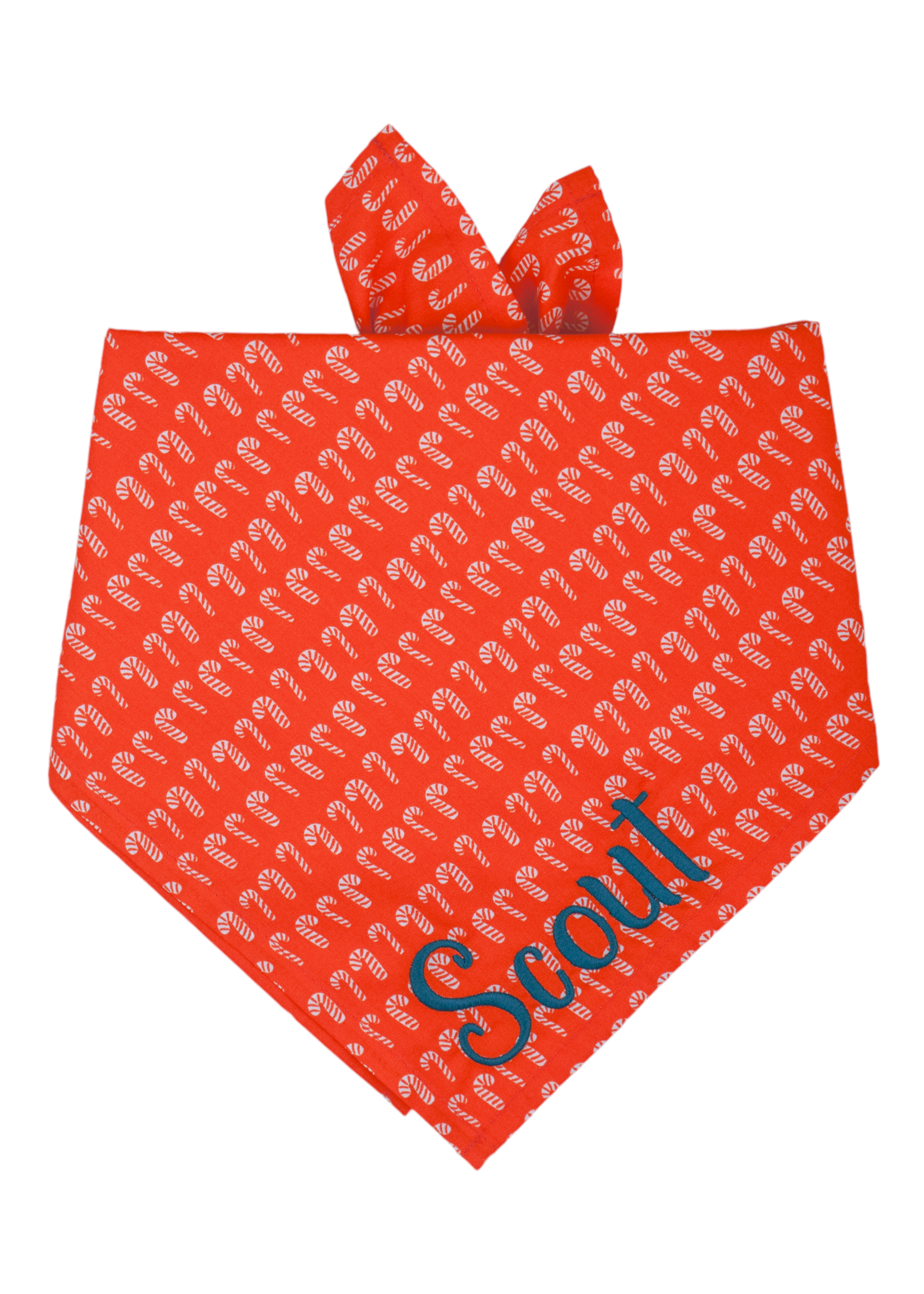 Christmas-themed dog bandana made from red fabric covered in a pattern of miniature candy cane illustrations. The bandana is folded like an inverted triangle and includes a folded edge at the top, designed for adjustable tying around a pet’s neck. The name "Scout" is embroidered on the bottom right.