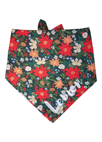 Holiday-themed dog bandana with a rich floral pattern that includes poinsettias, beautiful blossoms, pinecones, green sprigs, and scattered berries on a deep green background. The background enhances the festive tones, while the tie-back style offers an adjustable fit. The name "Lemon" is embroidered on the bottom right.