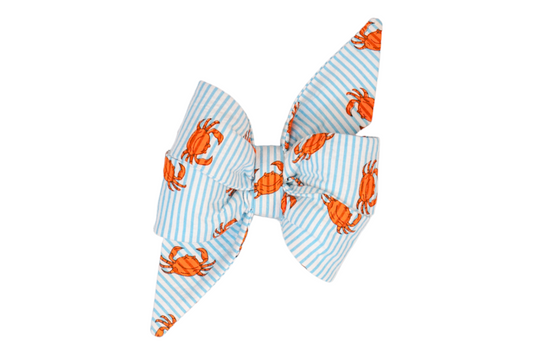 Close-up of a decorative feminine dog belle bow with a playful coastal theme, showcasing orange crab illustrations over crisp blue and white stripes. The bow has symmetrical loops and two long angled tails for a classic, polished look.