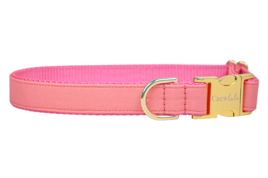 A solid coral dog collar with gold-tone hardware, including a side-release buckle engraved with “Crew LaLa” and a matching D-ring for leash attachment. The collar features a ribbed fabric exterior and durable pink webbing inside.