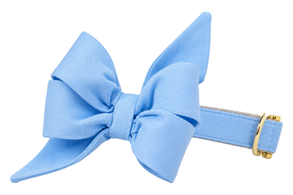 Dog collar featuring a large belle bow in Cornflower Blue fabric, a solid soft cornflower sky blue, attached to a matching Cornflower Blue collar with a nylon inner lining and gleaming gold hardware, including a D-ring and buckle.