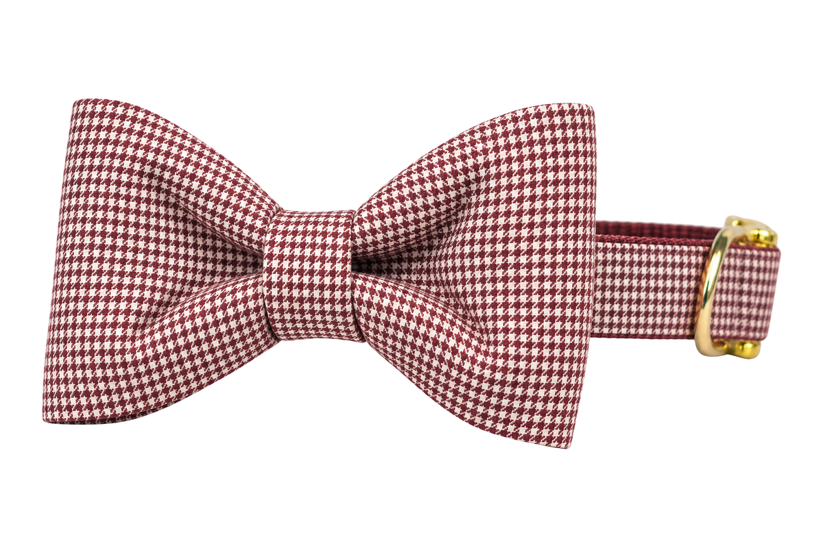Classic dog collar featuring a Crimson Houndstooth fabric bow tie, a fine burgundy and white houndstooth check, attached to a matching Crimson Houndstooth collar with a nylon inner lining and gleaming gold hardware, including a D-ring and buckle.