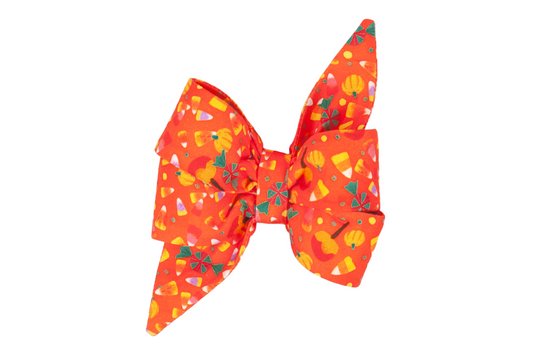 Bright orange dog belle bow with a fun Halloween design featuring colorful candy corn, tiny pumpkins, peppermint candies, and caramel apple illustrations. The oversized belle bow is double-layered with pointed tails, giving it a whimsical, festive flair ideal for dog costumes or fall photo ops.