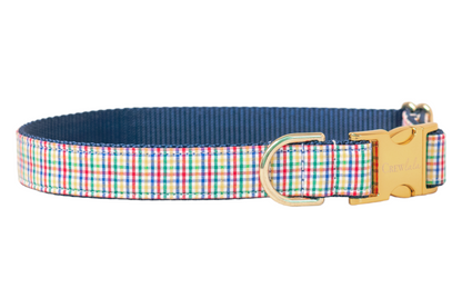Dog collar with a multicolor plaid fabric overlay stitched to nylon webbing. The collar includes a metal D-ring for leash attachment and a buckle engraved with "Crewlala" branding, blending style with durability.