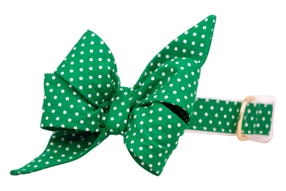 A bold green dog collar adorned with a large decorative feminine belle bow, both covered in evenly spaced white polka dots. The fabric belle bow has structured folds and long tails, creating a whimsical, eye-catching accessory. A gold buckle adds a touch of contrast and elegance.