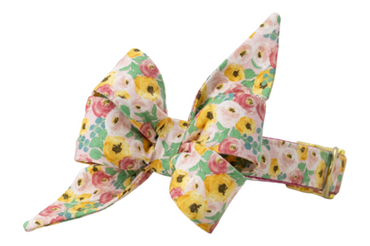Dog collar with an attached oversized belle bow, both made from cotton fabric featuring a vibrant floral print. The belle bow has an exaggerated structure with two tall, pointed loops and broad lower folds, giving it a sculpted, feminine silhouette. The collar is covered in matching floral fabric and secured with metal hardware, including an adjustment slider and D-ring.