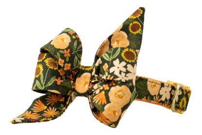 Floral dog collar with a large, pointed bow in earthy tones, decorated with blooming flowers and greenery on dark green fabric.