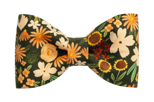 Pet bow tie featuring a garden-inspired design with warm-toned flowers and green leaves on deep green fabric.