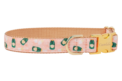 Durable and decorative dog collar in light pink, covered in a whimsical print of miniature champagne bottles and toasting glasses. The collar has a tan woven interior for added resilience, gold-colored metal hardware including a “Crewlala” logo buckle, and reinforced stitching along the fabric edges.