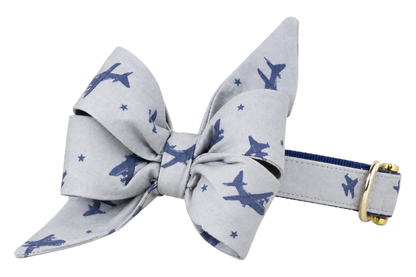 Dog collar featuring a large belle bow in Flying High fabric, a pale gray fabric with small slate blue airplanes and tiny stars, attached to a matching Flying High collar with a nylon inner lining and gleaming gold hardware, including a D-ring and buckle.
