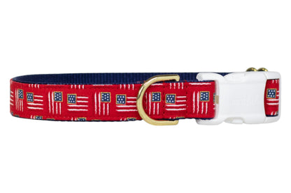 Patriotic-themed red dog collar with miniature American flags throughout, paired with a navy blue underside, a sturdy white buckle, and a gold metal D-ring for leash attachment.