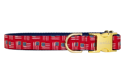 Patriotic-themed red dog collar with miniature American flags throughout, paired with a navy blue underside, a sturdy gold buckle, and a gold metal D-ring for leash attachment.