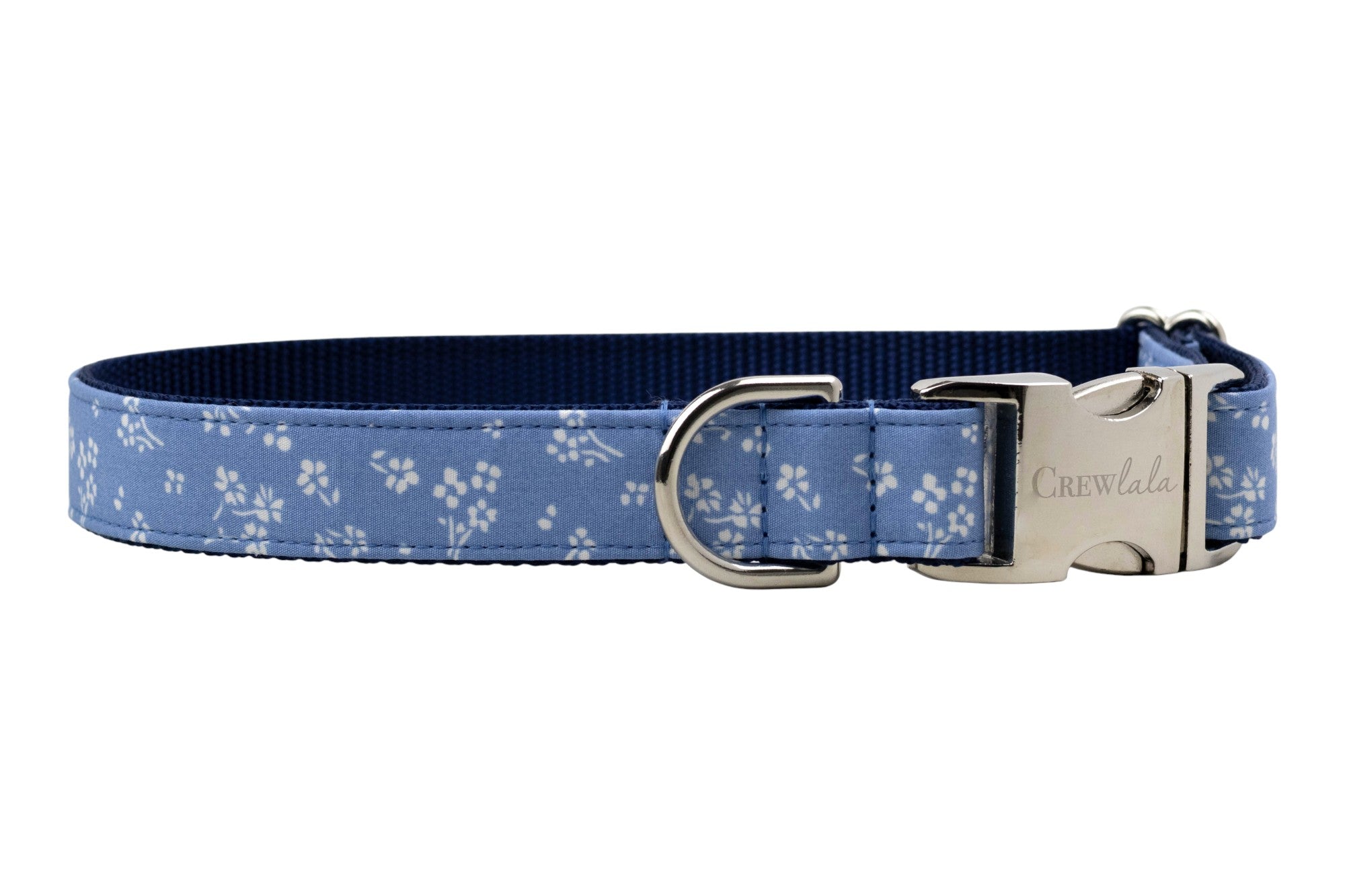 Close-up of a stylish dog collar featuring a soft blue fabric with tiny flowers, a polished silver side-release buckle engraved with “Crewlala,” and D-ring.
