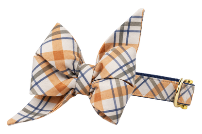 Dog collar featuring a large belle bow in Georgies Plaid fabric, a cream plaid with orange tan and slate gray stripes, attached to a matching Georgies Plaid collar with a nylon inner lining and gleaming gold hardware, including a D-ring and buckle.