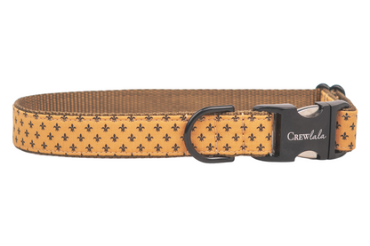 Stylish dog collar made from golden-yellow material with a repeating fleur-de-lis print, reinforced with nylon webbing, and fitted with metal hardware.
