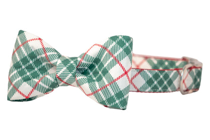 A festive dog collar featuring an attached matching bow tie with a green plaid pattern on a light fabric background. The bow tie is neatly tied in a classic symmetrical shape, and the collar includes  metal hardware for adjustment.