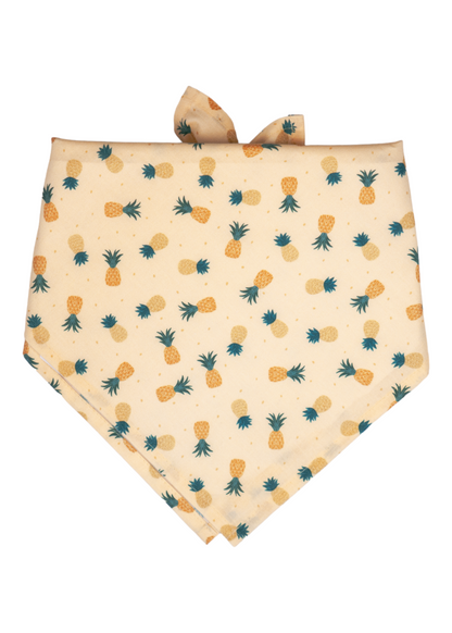 A soft yellow dog bandana decorated with a tropical pineapple pattern in muted yellow and orange shades, with dark green crowns. 