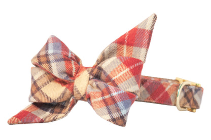 Adjustable dog collar with oversized belle bow in warm autumn plaid, crafted from soft flannel fabric with two large loops and pointed tails, attached to a matching collar with metal hardware. 