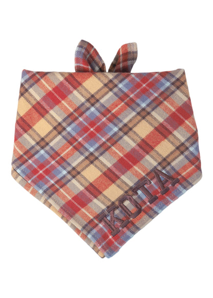 Cozy plaid dog bandana in warm fall hues, crafted from flannel fabric and accented with the name “KOTA” embroidered in dark thread at the bottom.