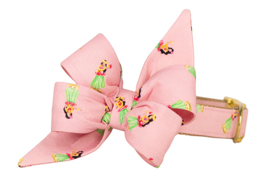 A tropical-themed pink belle bow tie collar for girl dogs, decorated with cute cartoon-style hula girls dancing in green skirts and bright tops.