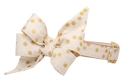 Ivory dog collar with an attached oversized belle bow made of matching fabric. Both the collar and the belle bow are covered in shiny polka dots, creating a coordinated and eye-catching design. The belle bow has crisp folds for a structured shape, while the collar is finished with detailed stitching and metal hardware.