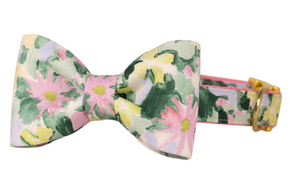 A dog bow tie made of fabric with a watercolor-style floral pattern in pastel pink, green, yellow, and lavender hues.