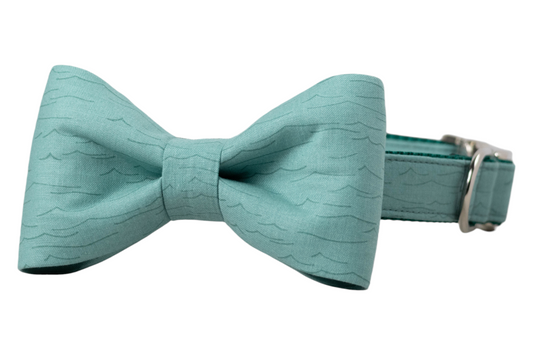 A minimalist teal dog collar with an attached matching bow tie, featuring subtle wavy textured lines and silver-tone metal hardware. 