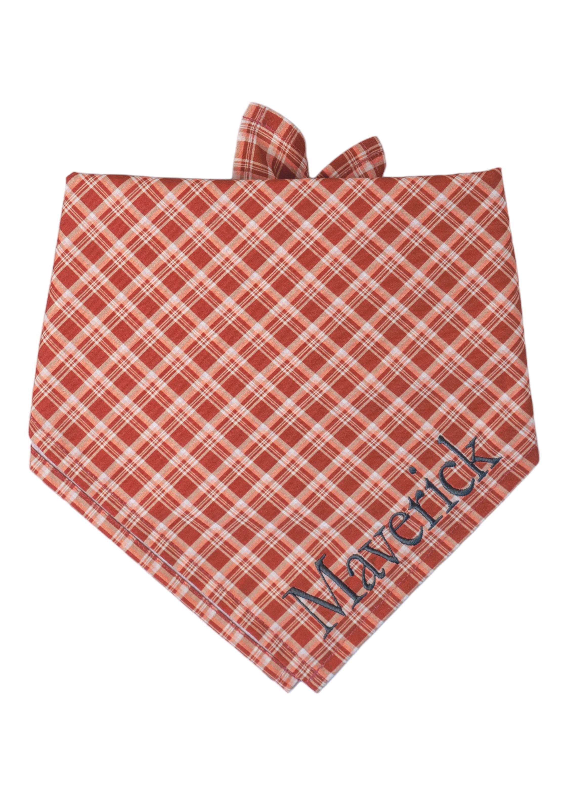 Personalized dog bandana in a diagonal red plaid pattern, tied at the top and embroidered with the name “Maverick” in bold lettering.