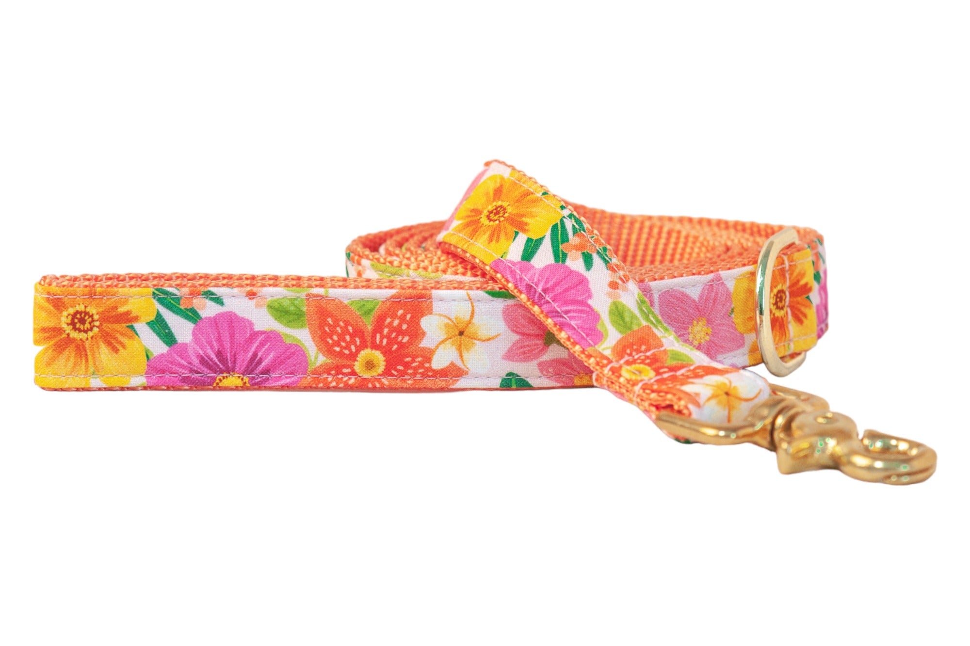 A dog leash with a bright tropical floral design featuring vivid orange, pink, yellow, and white flowers on a white background. The leash is lined with orange webbing and finished with a shiny gold clasp and ring.