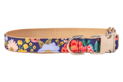 Floral fabric dog collar with a colorful botanical print on a navy background, including daisies, roses, and blossoms. The collar has webbing lining, a metal D-ring, and a matching buckle with the engraved “Crewlala” logo.