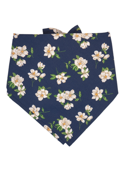 A navy blue triangular bandana decorated with an elegant pattern of white magnolia flowers and green leaves. The top corners are tied into soft, ear-like points.