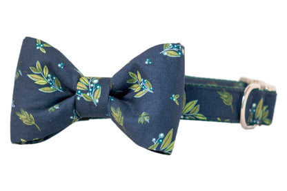 Navy blue dog collar with an attached matching bow tie, decorated with a pattern of leafy branches and small pale berries, featuring an adjustable collar and metal hardware.
