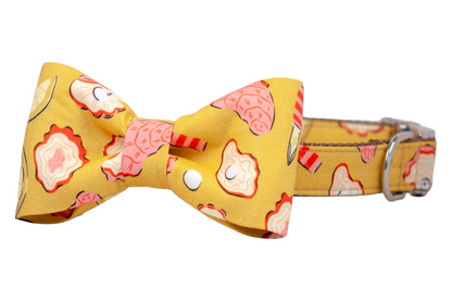 Yellow fabric collar featuring a quirky coastal pattern with oyster shells, lemon wedges, pearls, and seafood tools. The matching bow tie is centered on the adjustable collar with metallic hardware.