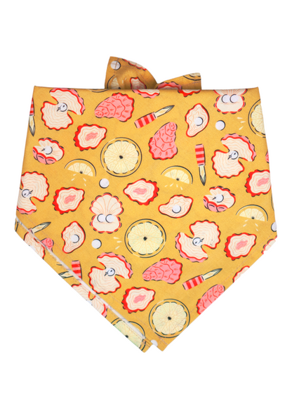 Bright yellow dog bandana decorated with a seafood pattern of illustrated oysters in pink and cream tones, alongside pearls, halved lemons and tiny oyster knives. 