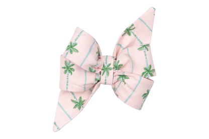 Tropical-themed dog belle bow, made from pastel pink fabric patterned with palm trees and light aqua blue stripes, styled with pointed tails and a voluminous structure.
