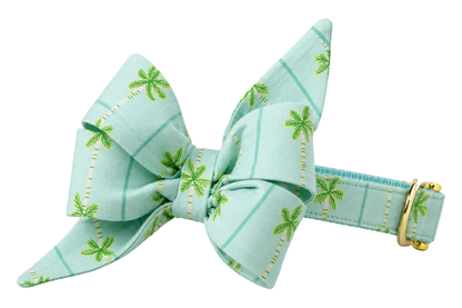 Dog collar featuring a large belle bow in Palm Springs fabric, a pale mint aqua windowpane fabric with small green palm trees, attached to a matching Palm Springs collar with a nylon inner lining and gleaming gold hardware, including a D-ring and buckle.
