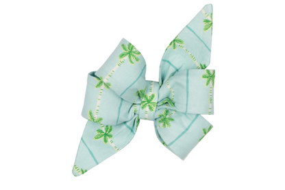 Tropical-style girl dog belle bow in pastel aqua blue, featuring a green palm tree and blue stripe pattern with long pointed ends and layered folds.