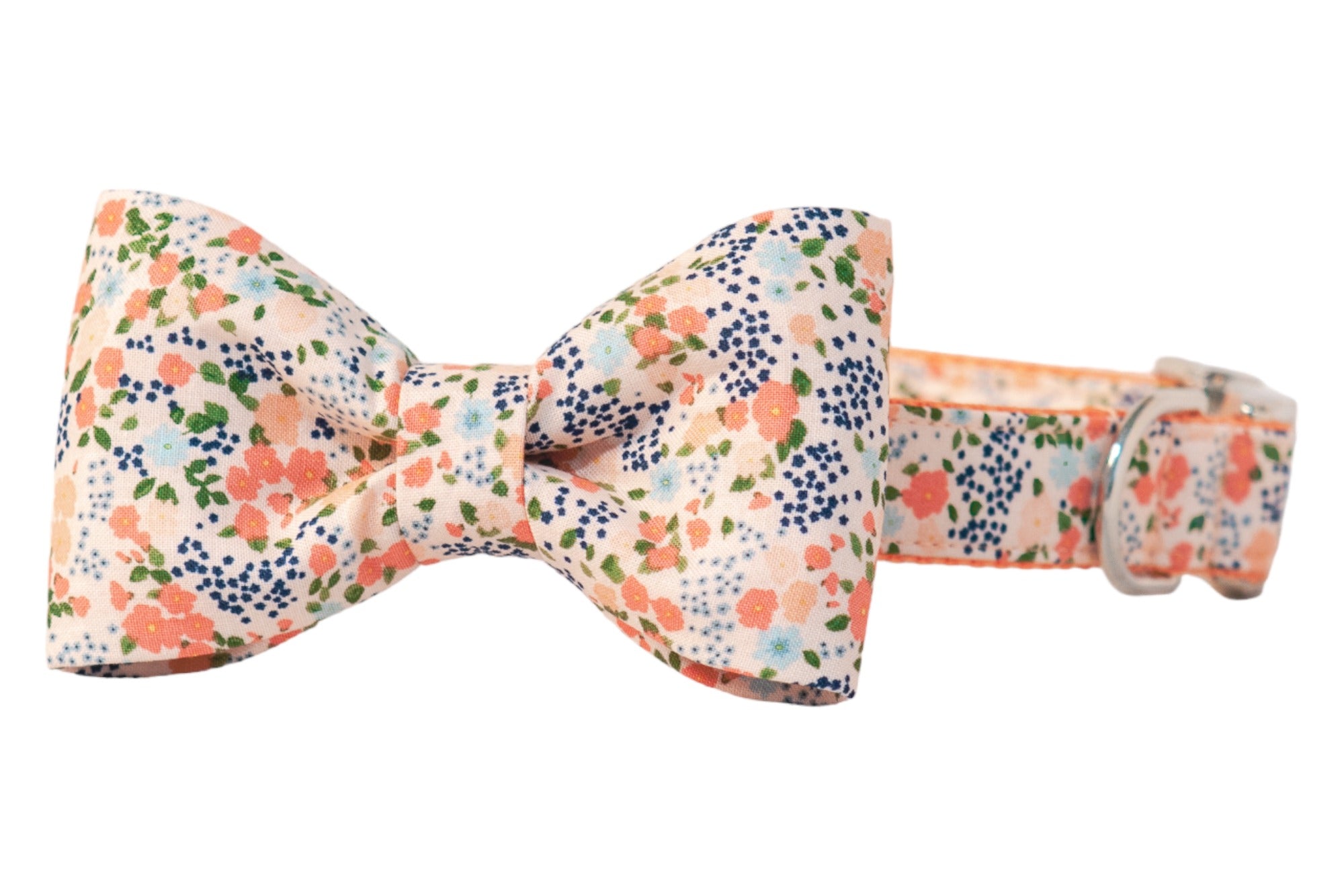 Dog collar with an attached matching bow tie in a peachy pink fabric patterned with floral clusters and leaves, secured with metal hardware.