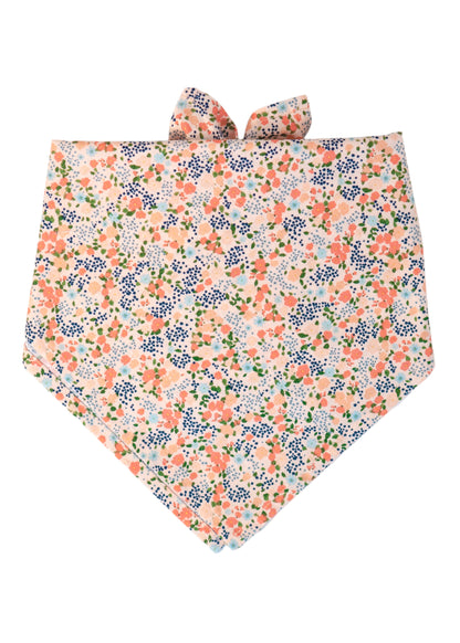 Dog bandana in pale peachy pink fabric, covered in a dense floral print with green foliage, designed to tie around the neck. 