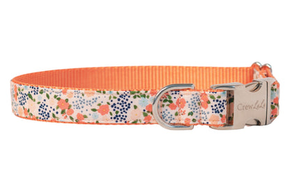 Stylish floral dog collar with peach and pink blooms scattered among leaves, contrasted by vivid peach nylon lining, and secured with metal hardware engraved with the brand name Crewlala.