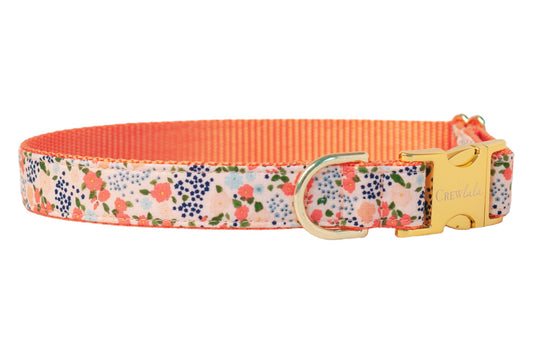 Stylish floral dog collar with peach and pink blooms scattered among leaves, contrasted by vivid peach nylon lining, and secured with metal hardware engraved with the brand name Crewlala.
