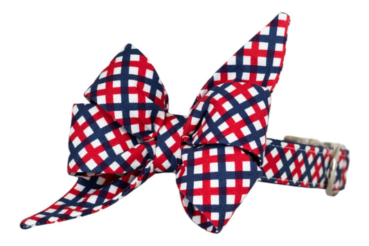 Patriotic-themed dog collar with a decorative belle bow, featuring a red, white, and blue plaid design. The collar includes an adjustable silver buckle for secure fastening.